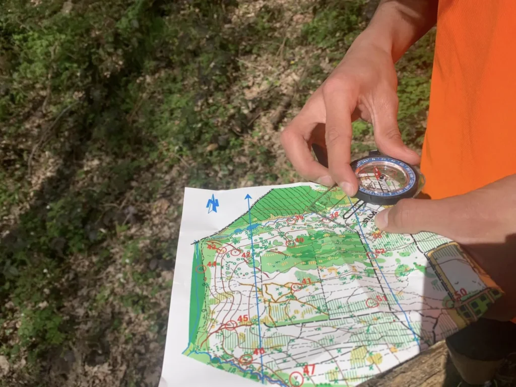 Carte et boussole en main devant une balise de course d'orientation